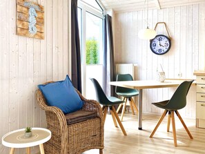 A room with a wicker chair, a table, and chairs, a clock, and a window with curtains.