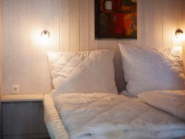 Una cama con ropa de cama blanca y dos luces fijadas a la pared.
