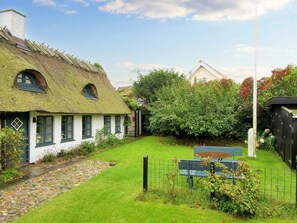 A thatched-roof cottage with a stone pathway leading to a bench.