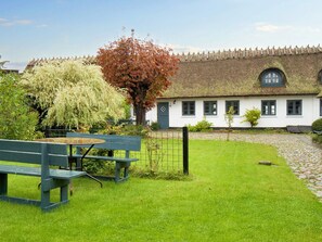 A traditional white building with a thatched roof, a small garden with a bench, and a tree with autumn leaves.
