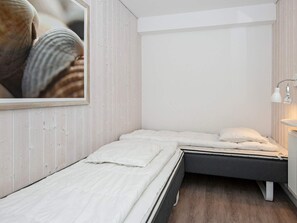 A bedroom with two beds, a wooden floor, and a white wall.