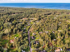 Ilmakuva asuinalueesta, jossa talot ovat tiheän metsän ympäröimiä. Taustalla näkyy selkeä tie ja vesistö.