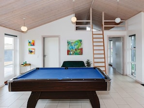 A pool table in a room with a sloped ceiling, wooden beams, and a ladder. There are two paintings on the walls, a door, and a window with a view. - 5 Star Holiday Home in Lokken (Lokken)
