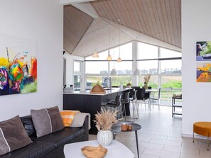 A modern living room with a black leather sofa, a white coffee table, and a dining area with a black table and chairs. - 5 Star Holiday Home in Lokken (Lokken)
