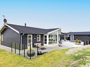 A modern house with a large glass front, a covered patio, and a well-maintained lawn. - 5 Star Holiday Home in Lokken (Lokken)