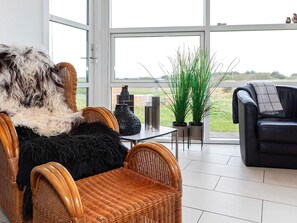 A modern living room with wicker furniture, a black leather sofa, and a view of the outdoors.