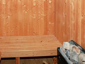 A wooden bench with a metal frame, a wooden wall with vertical planks, and a black bin filled with rocks. - Holiday Home in Gelting (Gelting)