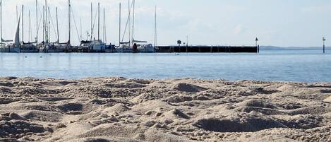 A sandy beach with a row of sailboats docked at a pier.