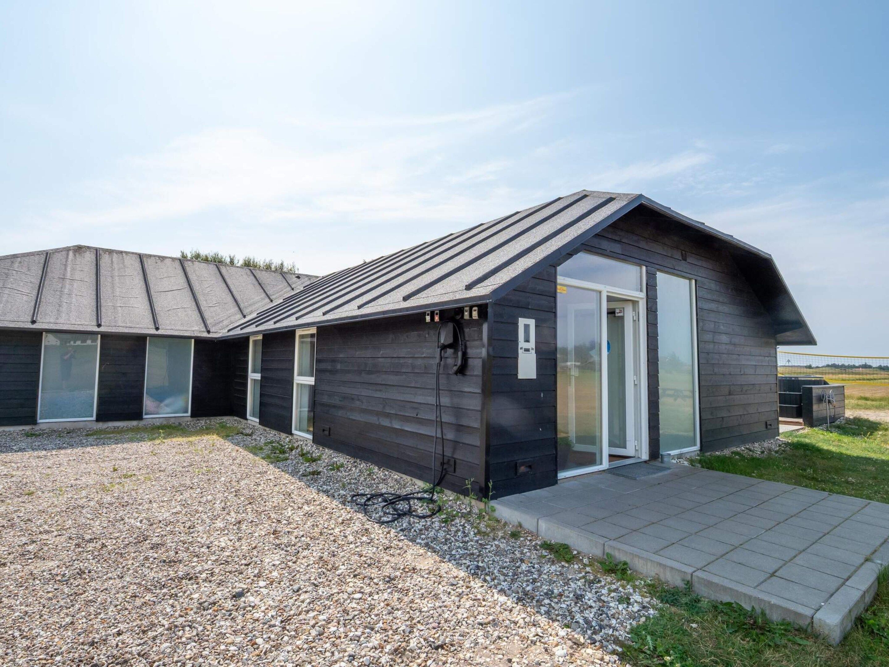 A modern building with a sloped roof, large windows, and a gravel driveway.