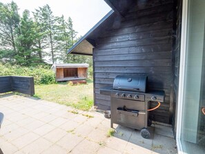 An outdoor grill area with a built-in oven, a wooden structure in the background, and a paved patio.