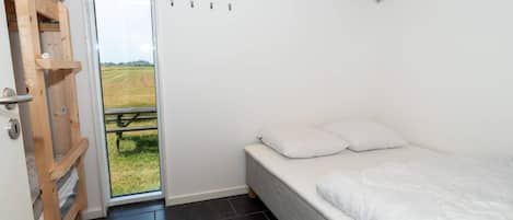 Une chambre à coucher avec un lit, une échelle en bois et une porte donnant sur un espace extérieur.