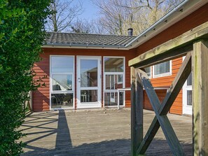 A wooden deck leading to a red building with large windows and a white door.