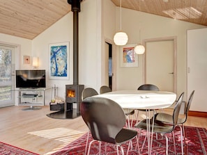 A modern living room with a fireplace, a dining area with chairs, a television, and artwork on the walls.