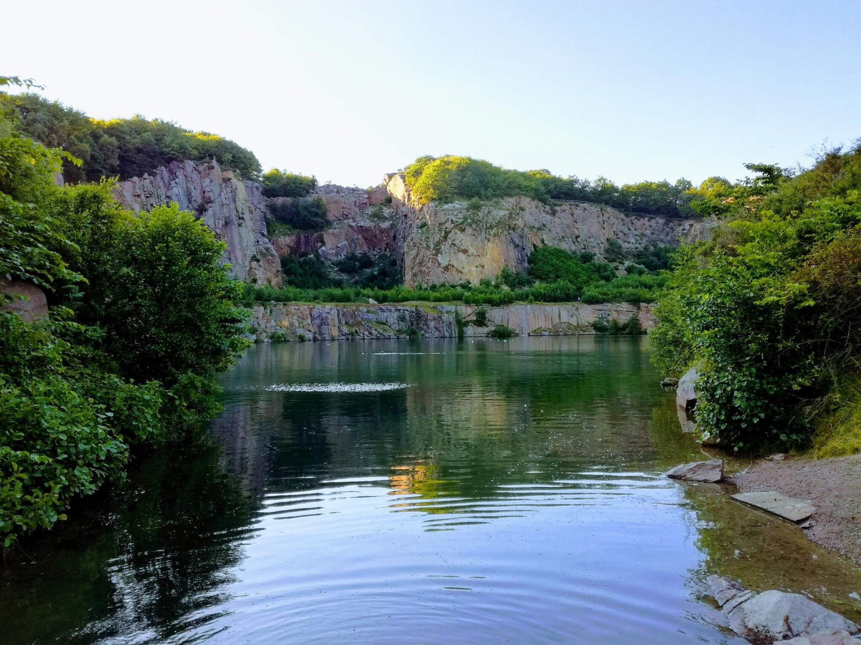 A calm river with rocky cliffs and dense greenery on both sides.