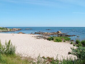 A sandy beach with rocky outcrops and greenery in the foreground.