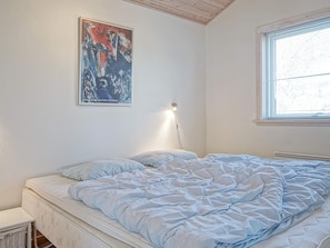 A bedroom with a bed, a wall-mounted light, a window, and a painting.