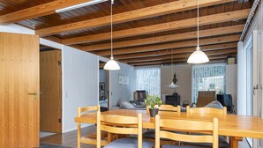 Un coin repas avec une table et des chaises en bois, un luminaire suspendu et une vue sur le salon.