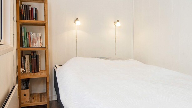 Une chambre avec un lit simple, une bibliothèque en bois et deux lampes fixées au mur.