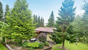 Ein Haus mit rotem Ziegeldach, umgeben von einem gepflegten Garten mit verschiedenen Bäumen und Sträuchern.