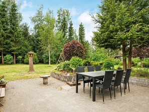 Eine Terrasse im Freien mit Tisch und Stühlen, umgeben von einem Garten mit verschiedenen Pflanzen und einem Vogelfutterhaus.