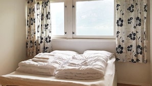 Un llit amb roba de llit blanca i un matalàs, una finestra amb vistes i cortines florals.