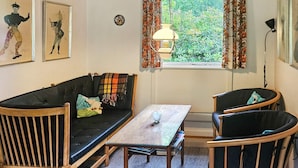 Una habitación acogedora con un sofá de madera, dos sillones, una mesita y una ventana con cortinas.