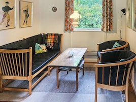 Una habitación acogedora con un sofá de madera, dos sillones, una mesita y una ventana con cortinas.