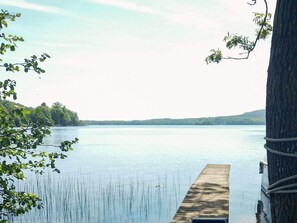 Un lac paisible, avec une jetée en bois qui s’avance sur l’eau, entouré d’arbres et bordé, au loin, par une rive.