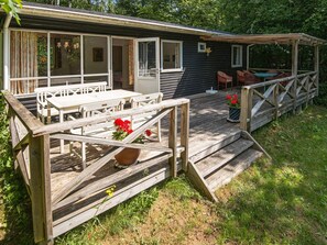Une terrasse en bois avec des sièges extérieurs, un espace couvert avec des chaises et un escalier menant à un bâtiment.