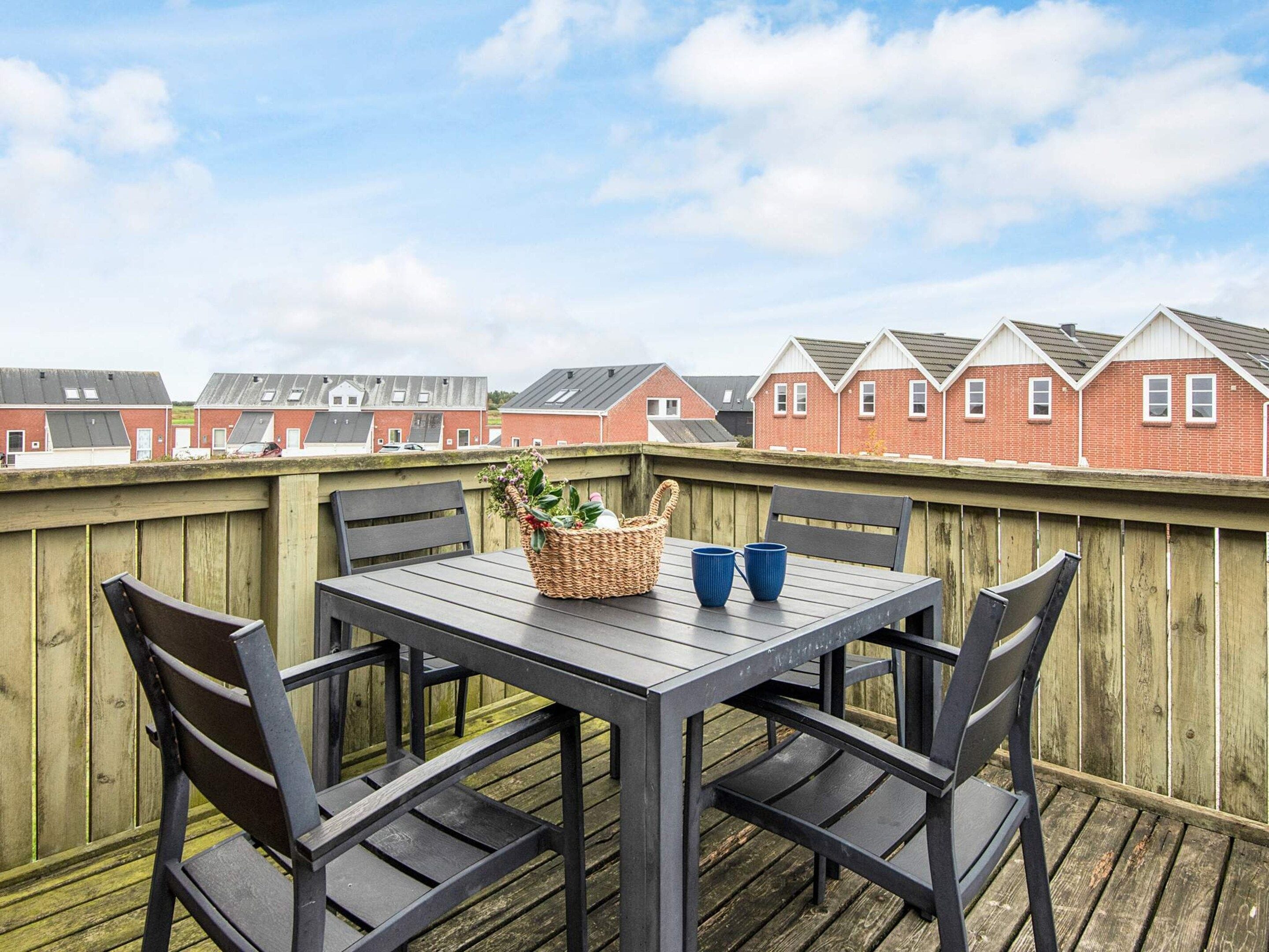 Eine Holzdielen-Terrasse mit Tisch, Stühlen, einem Korbwägelchen und zwei blauen Tassen.