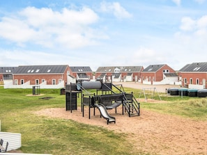 A playground with a slide and climbing structures, surrounded by a grassy area and red brick buildings with white trim. - 4 Person Holiday Home in Romo-by Traum (Rømø)