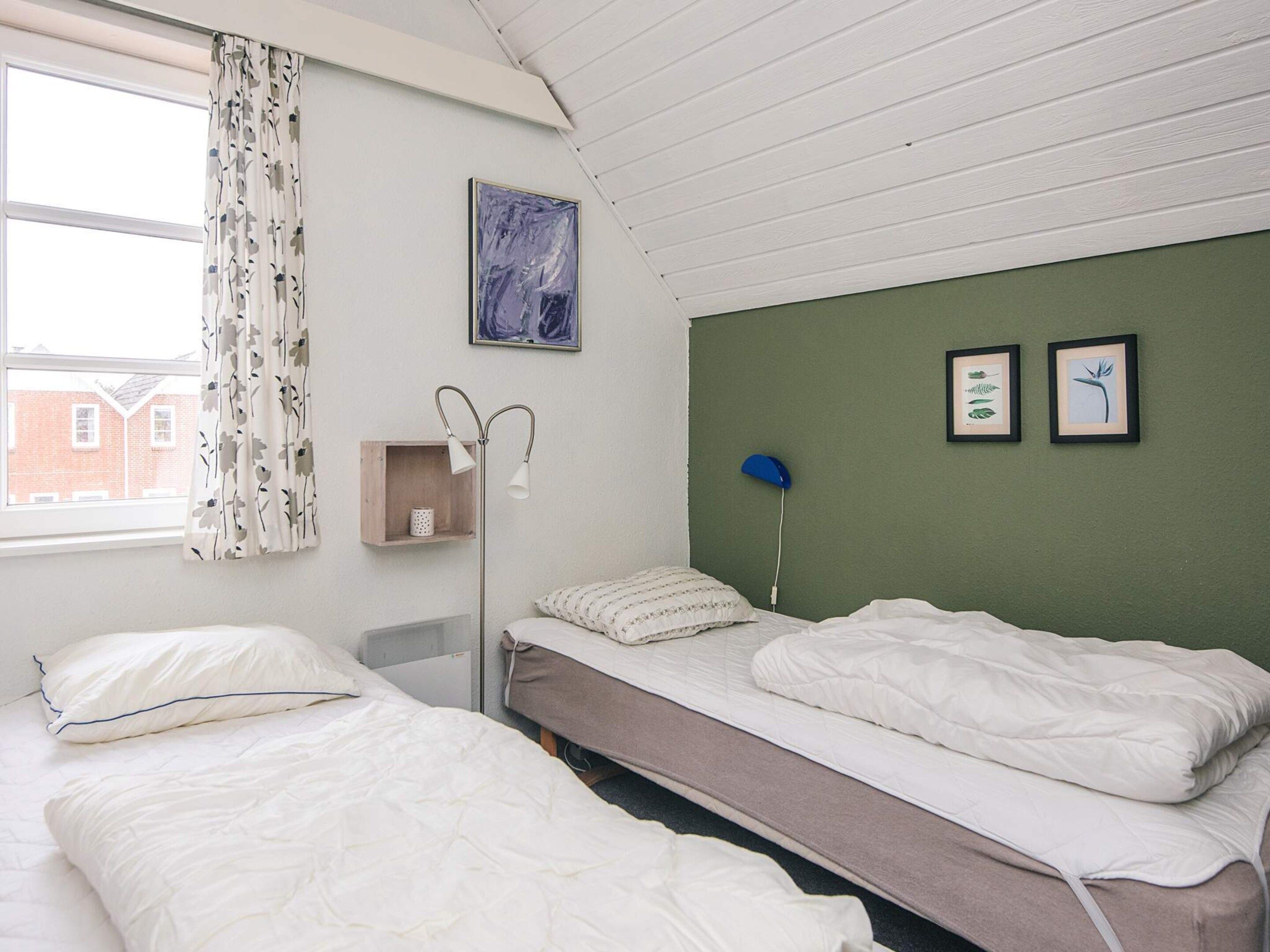 A room with two beds, a bedside table, a lamp, and a window with curtains.