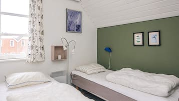 A room with two beds, a bedside table, a lamp, and a window with curtains.