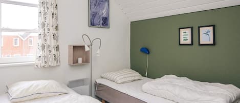 Quarto com duas camas, uma mesinha de cabeceira, uma luminária e uma janela com cortinas.