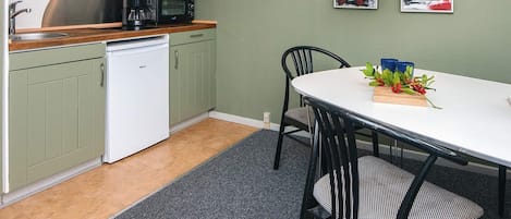A compact kitchen with a dishwasher, a microwave, and a coffee maker on the counter. There is a dining table with chairs and a small plant on the table.