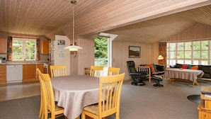 Ett rymligt rum med ett träpanelat tak, en matplats med bord och stolar, en soffa och ett litet bord med en lampa.