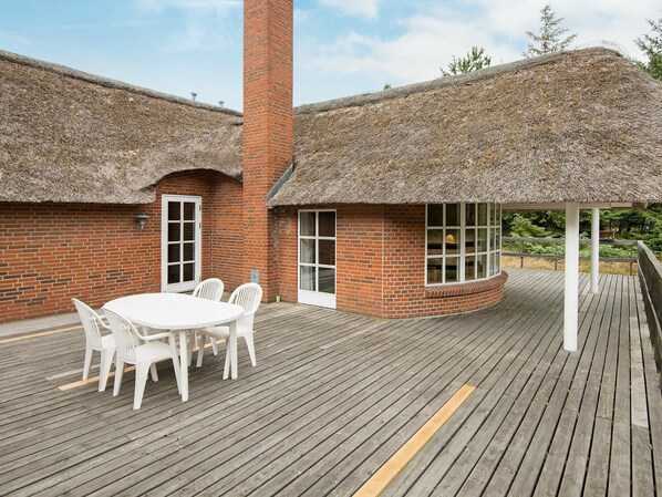 A brick building with a thatched roof, a wooden deck, and a white table with chairs. - Comfortable Holiday Home in Rømø With Sauna (Rømø)