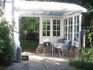 A covered patio with a table and chairs, surrounded by greenery.