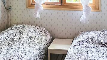 A room with two beds, a small table, and a window with lace curtains.