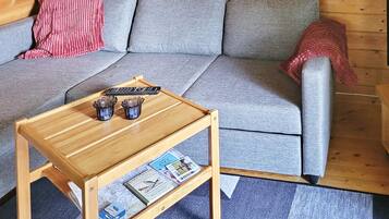 A wooden coffee table with a magazine and remote controls on it, placed in front of a grey sofa with a red blanket.