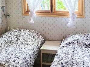 A room with two beds, a small table, and a window with lace curtains. - 3 Person Holiday Home in Vastervik (Vastervik)