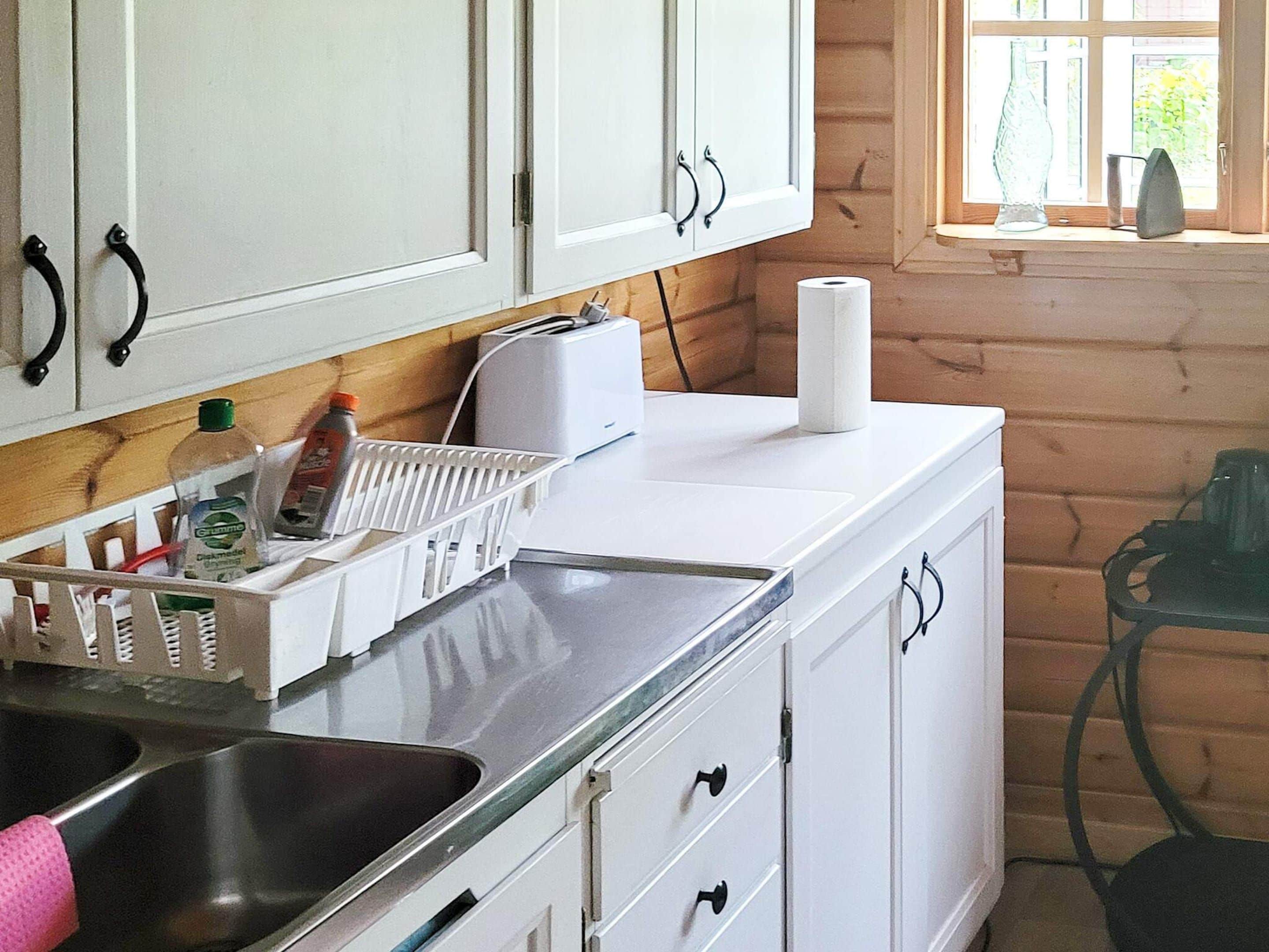 A kitchen with white cabinets, a stainless steel sink, and a window with a view of greenery.