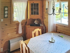 A wooden cabin interior with a dining table, chairs, a radiator, a cabinet with a lamp, and a window with curtains. - 3 Person Holiday Home in Vastervik (Vastervik)