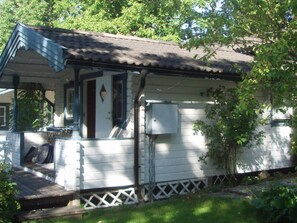 A small, single-story house with a porch, a chimney, and a utility box.