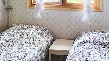 A room with two beds, a small table, and a window with lace curtains.