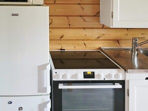 A kitchen with a white refrigerator, a stove with a digital display, and wooden paneling on the wall. - 3 Person Holiday Home in Vastervik (Vastervik)