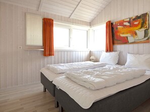 A double bed with white bedding, a grey headboard, and a window with orange curtains.