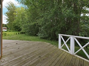 A wooden deck with a white railing, surrounded by lush greenery and trees.