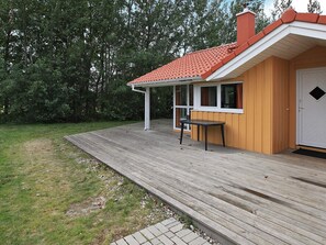 A wooden deck with a table and chairs, a covered porch, and a house with a red roof. - Holiday Home in GrÃ¶mmitz (Groemitz)