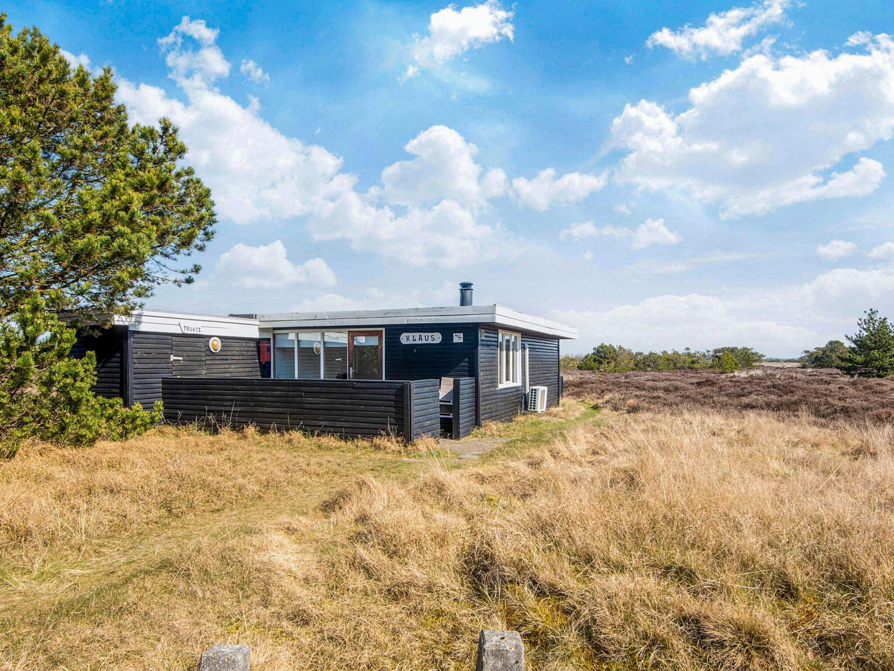 A cabin with a dark exterior, a visible chimney, and a window with a view of the surrounding landscape.